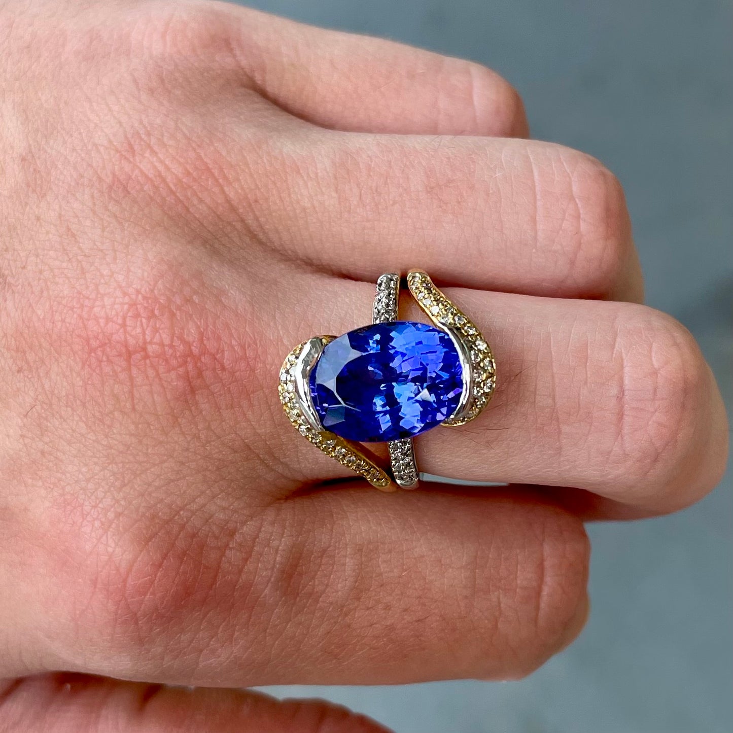 A large, oval cut blue tanzanite set in a two tone yellow and white gold diamond ring.