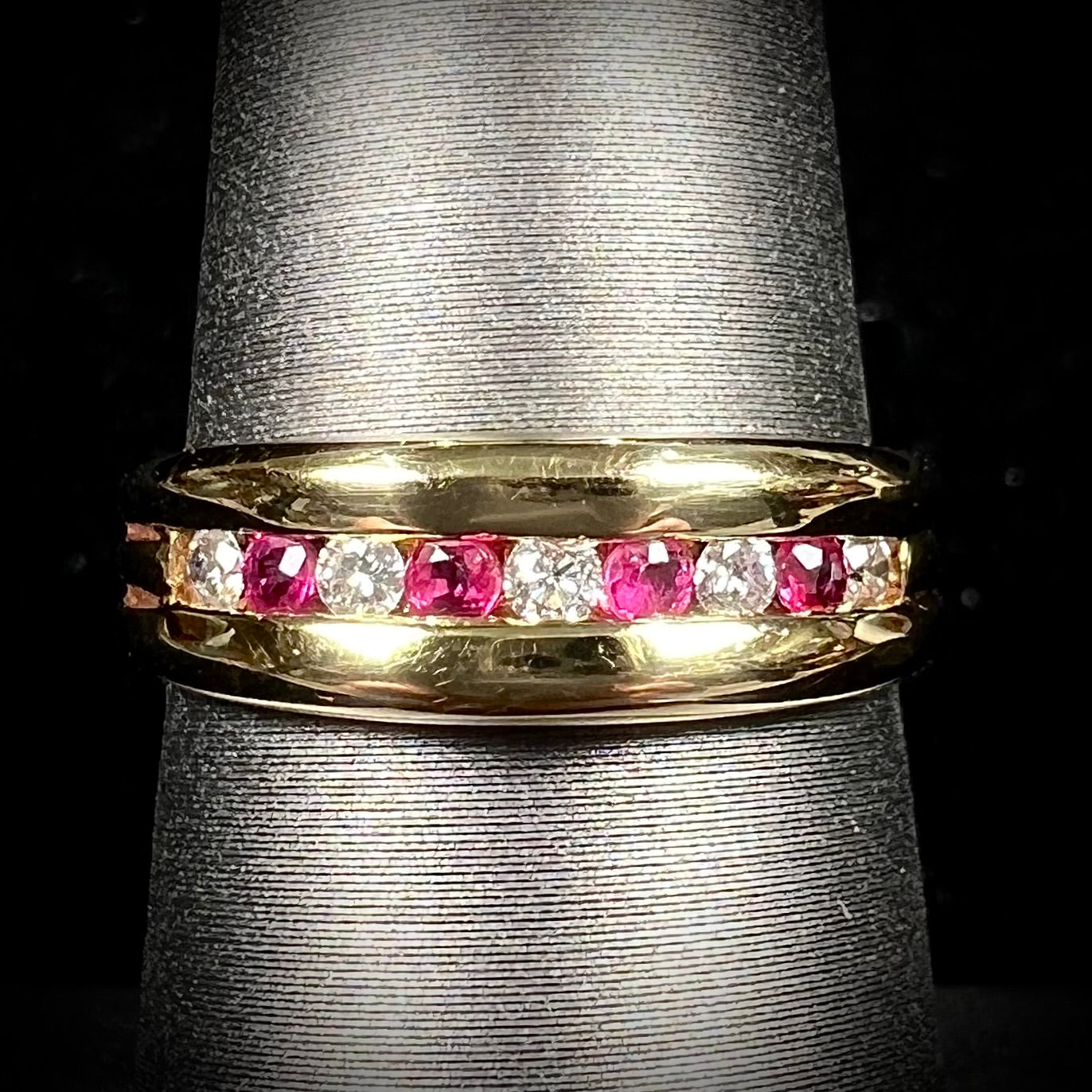 An 18kt yellow gold band channel set with round cut rubies and diamonds.