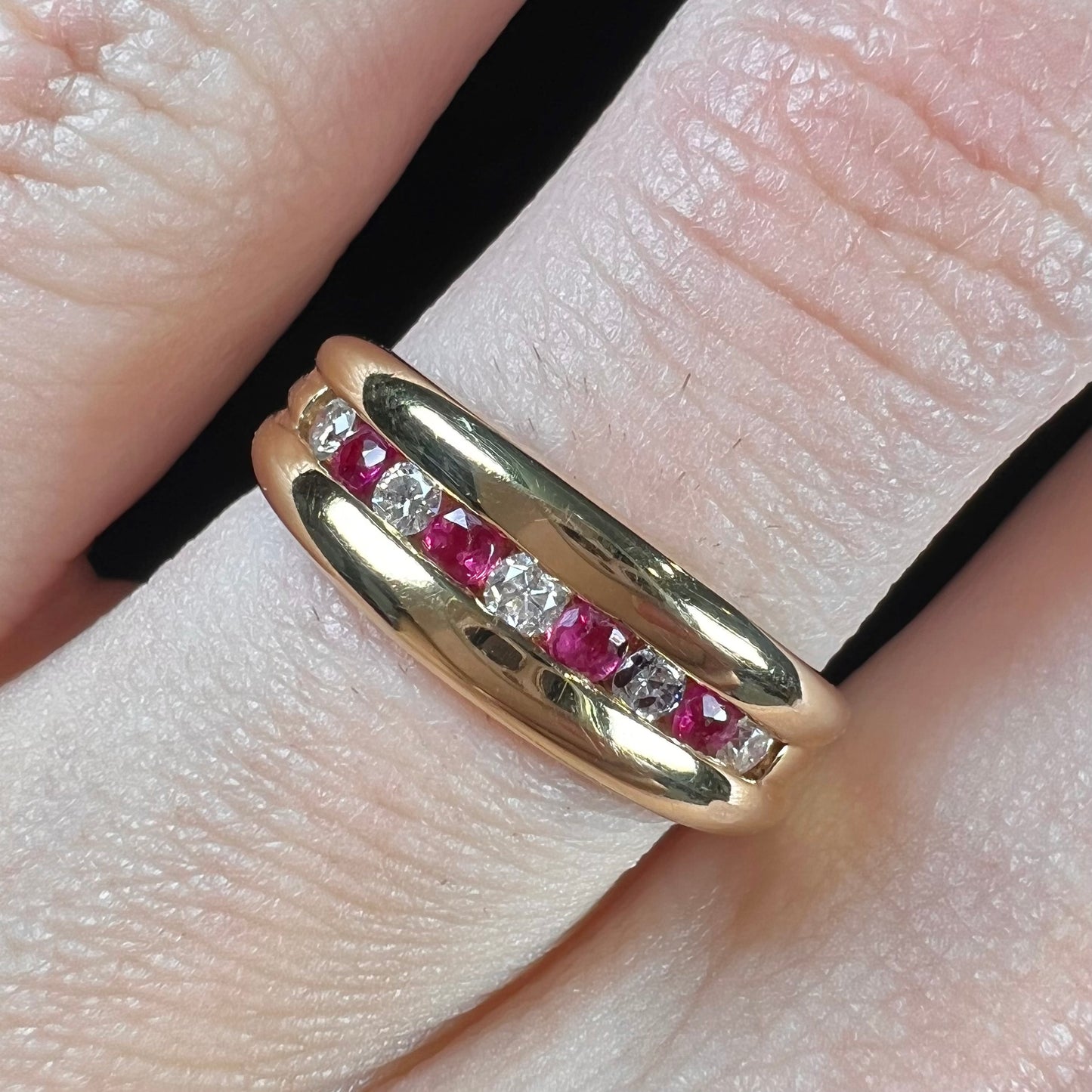 An 18kt yellow gold band channel set with round cut rubies and diamonds.