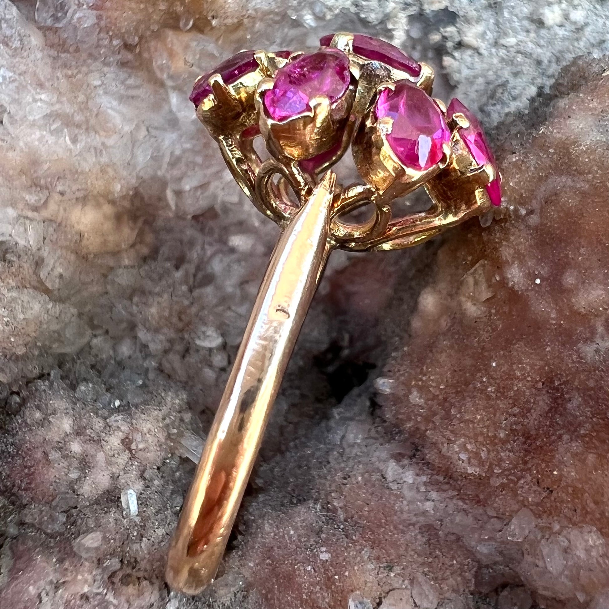 A yellow gold pink Burma ruby cluster ring with a faceted oval center stone surrounded by marquise cut stones.