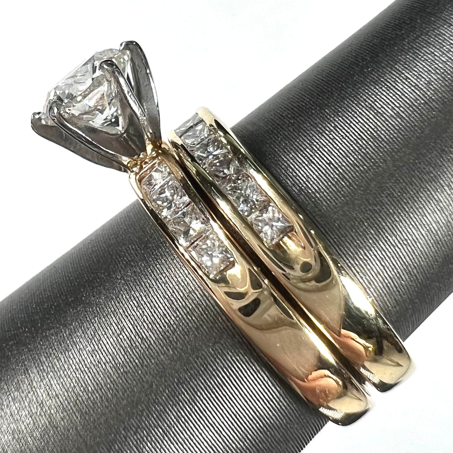 A diamond engagement and wedding ring set. The center stone is a 1 carat round diamond, and the side stones are channel set princess cut diamonds.