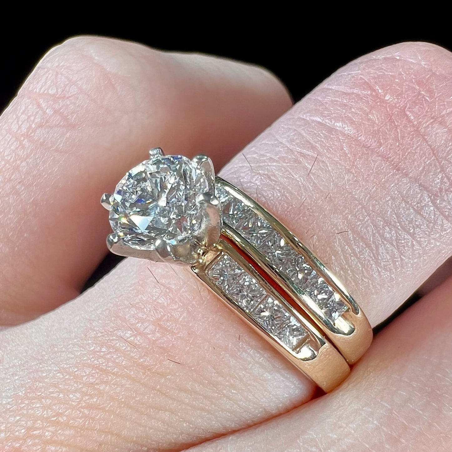 A diamond engagement and wedding ring set. The center stone is a 1 carat round diamond, and the side stones are channel set princess cut diamonds.