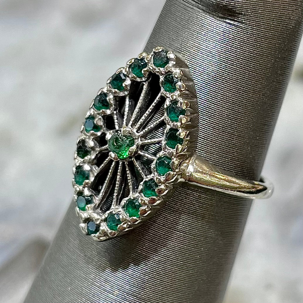 A vintage marquise shape white gold ring set with a halo of round cut emeralds around a single center stone.