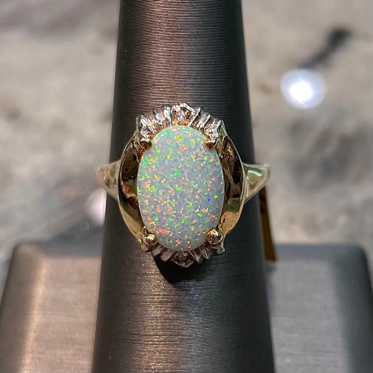 A yellow gold ring set with a synthetic, lab created white opal and two natural diamond accents.