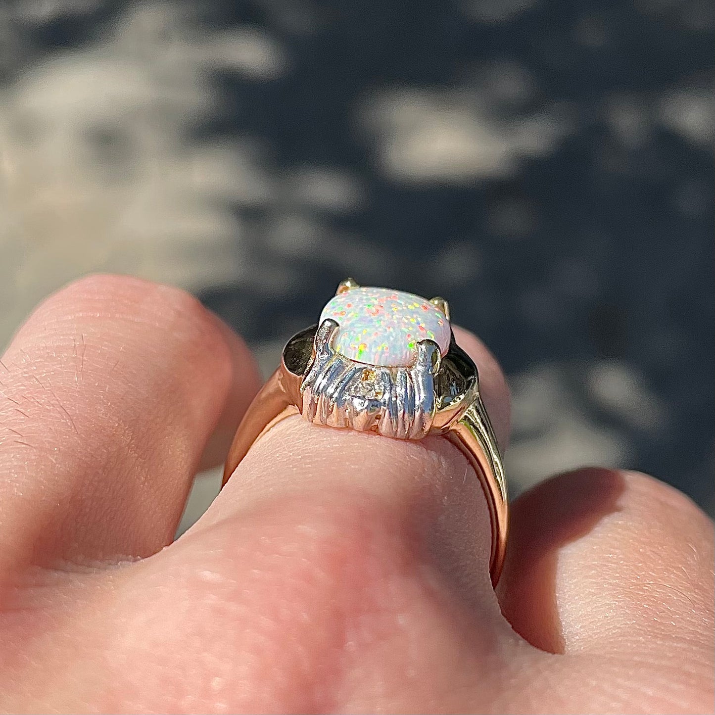A yellow gold ring set with a synthetic, lab created white opal and two natural diamond accents.