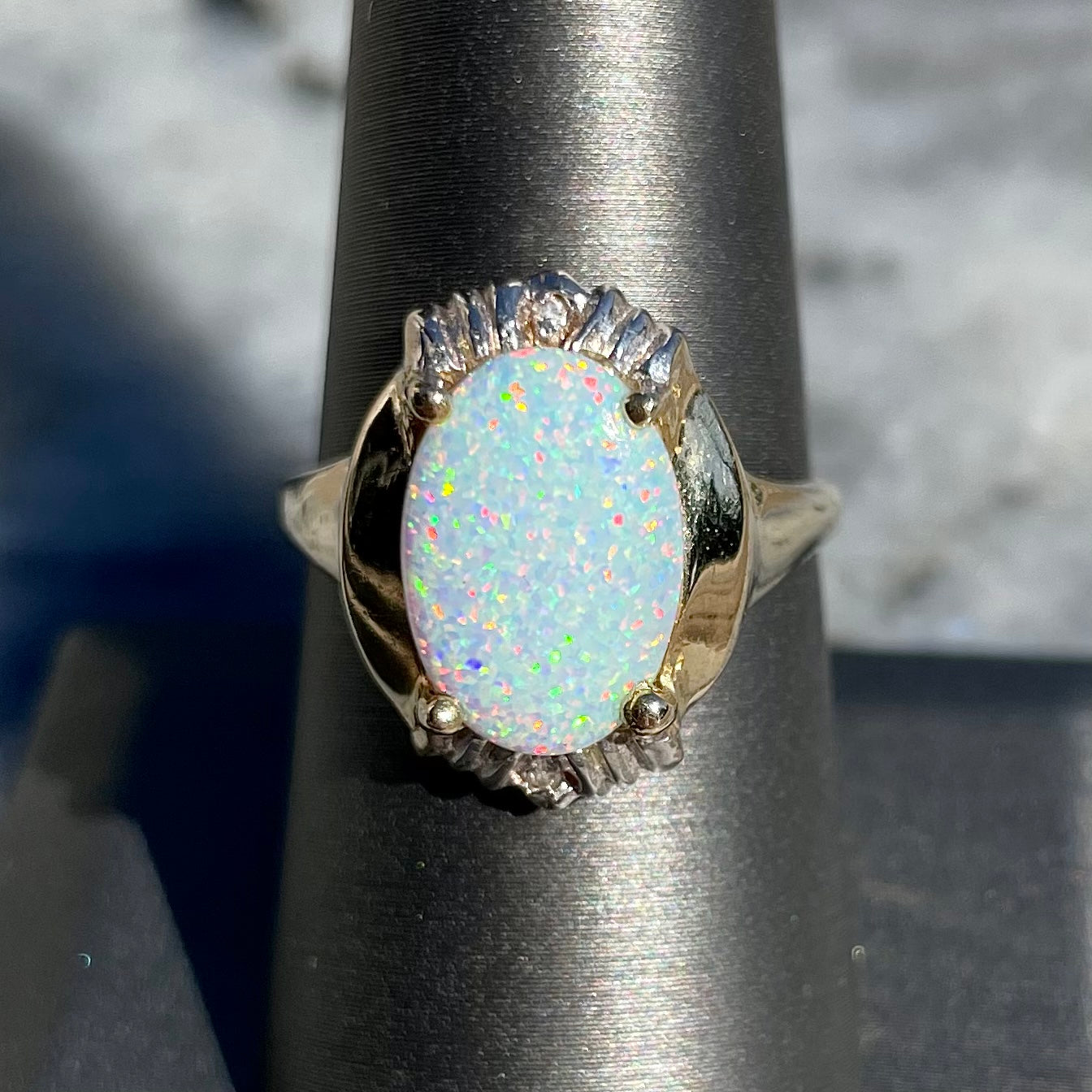 A yellow gold ring set with a synthetic, lab created white opal and two natural diamond accents.