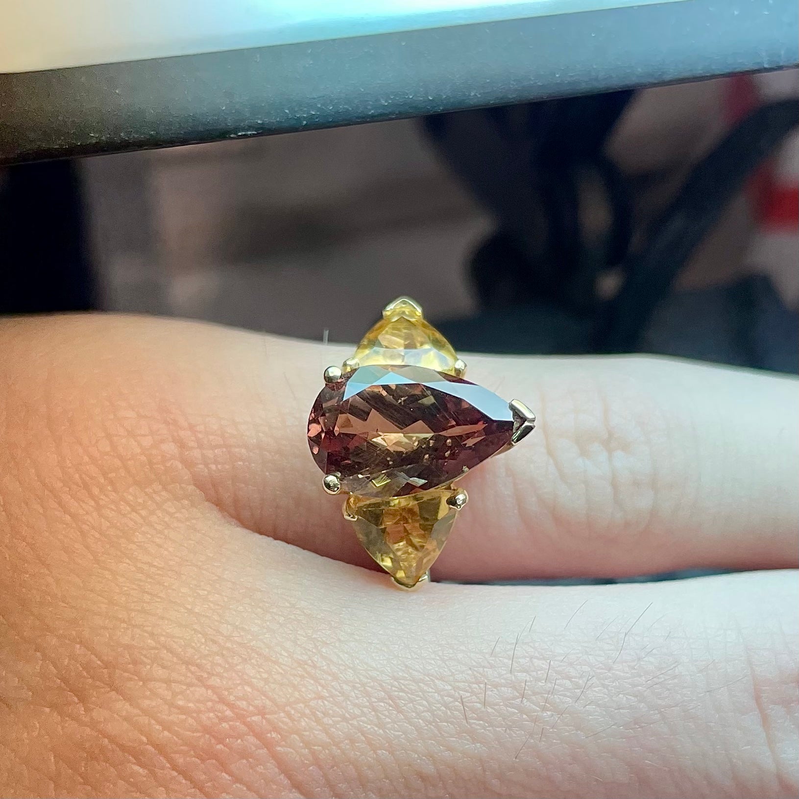 A gold ring set with a pear shape color change garnet between two trillion cut citrine accent stones.