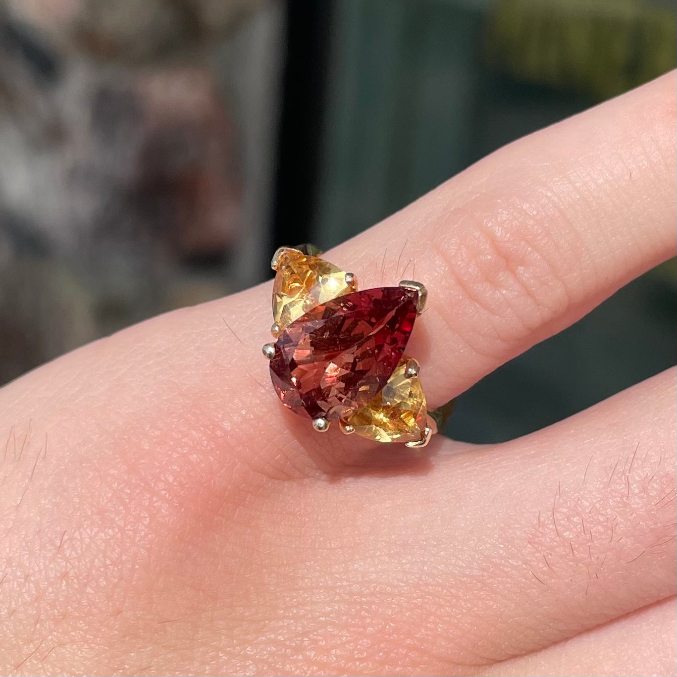 A gold ring set with a pear shape color change garnet between two trillion cut citrine accent stones.