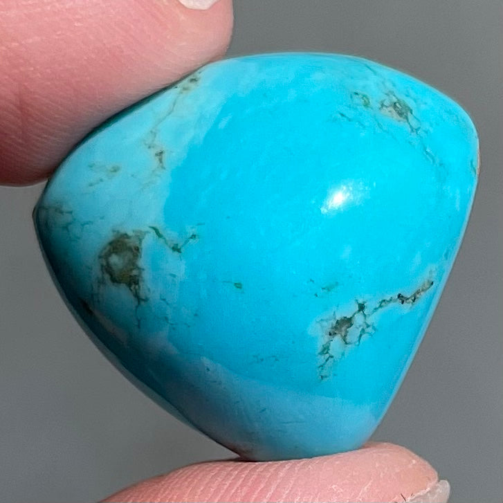 A loose, triangular cabochon cut blue turquoise stone from Sleeping Beauty Mine, Arizona.