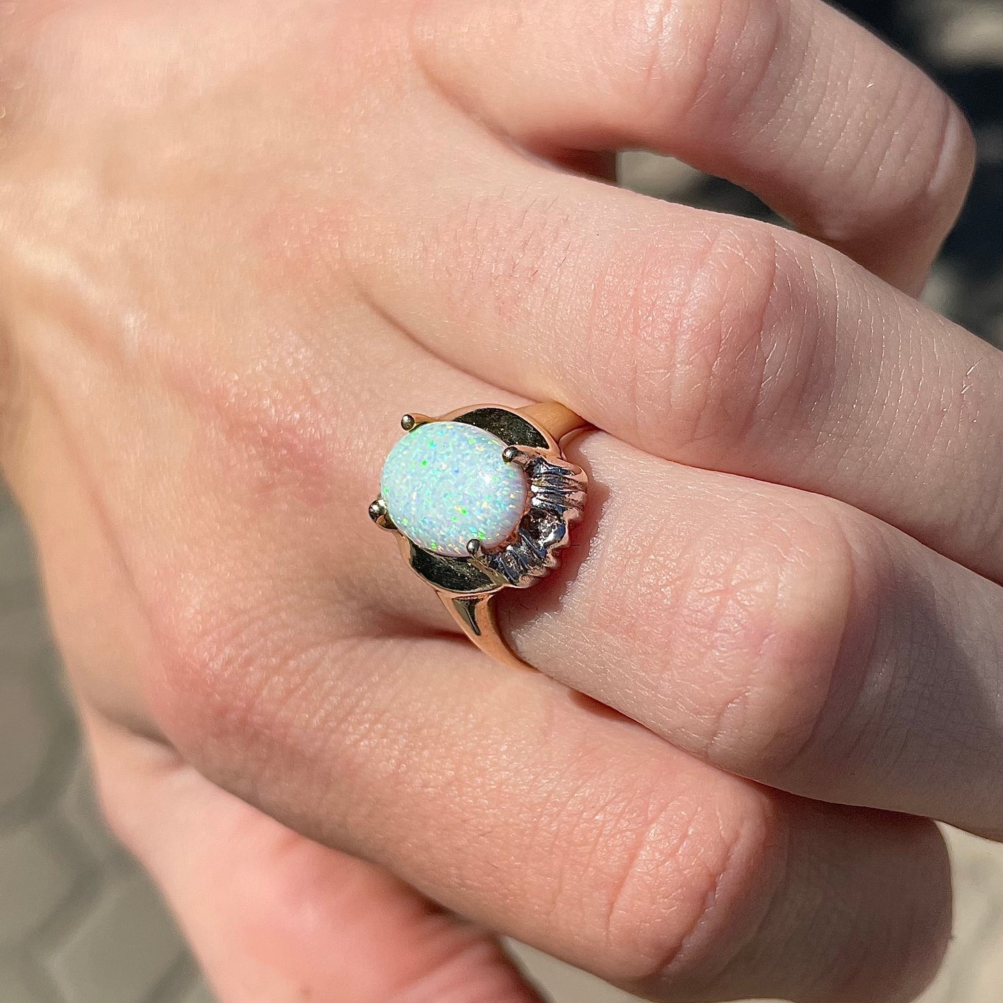 A yellow gold ring set with a synthetic, lab created white opal and two natural diamond accents.