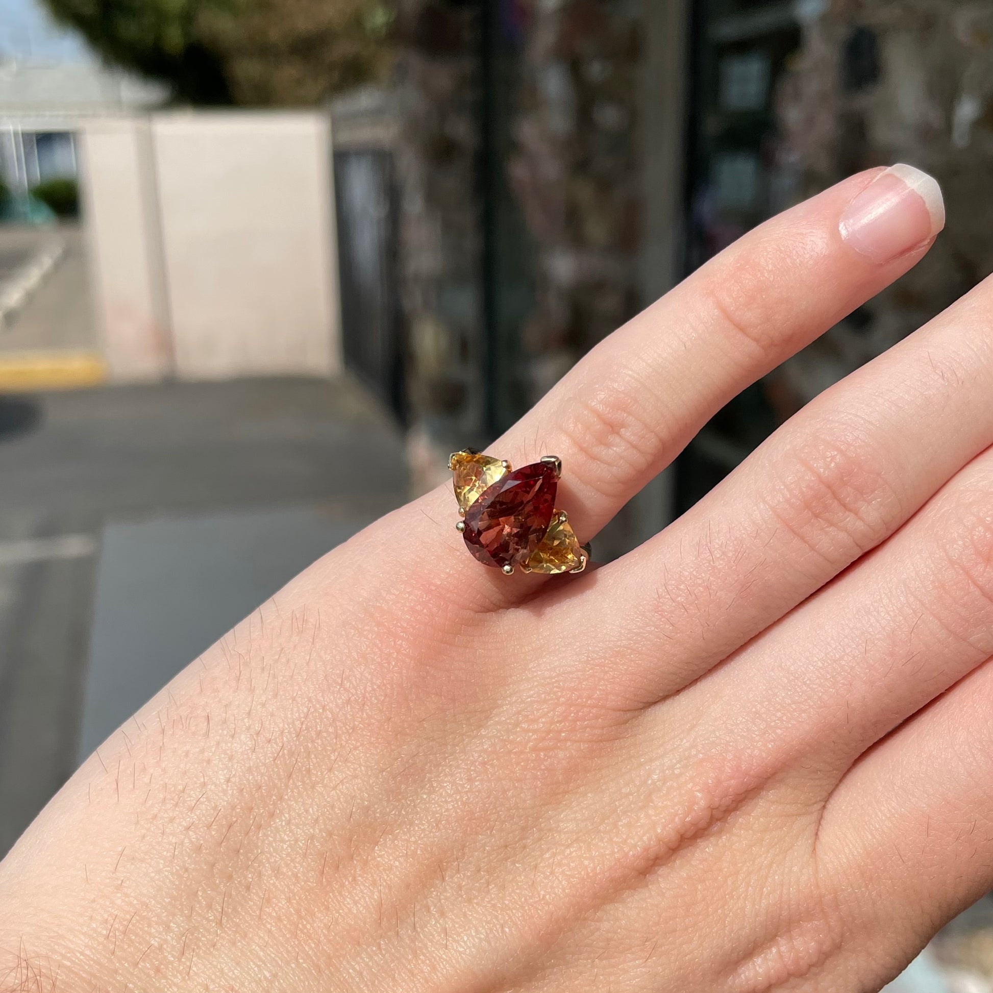 A gold ring set with a pear shape color change garnet between two trillion cut citrine accent stones.