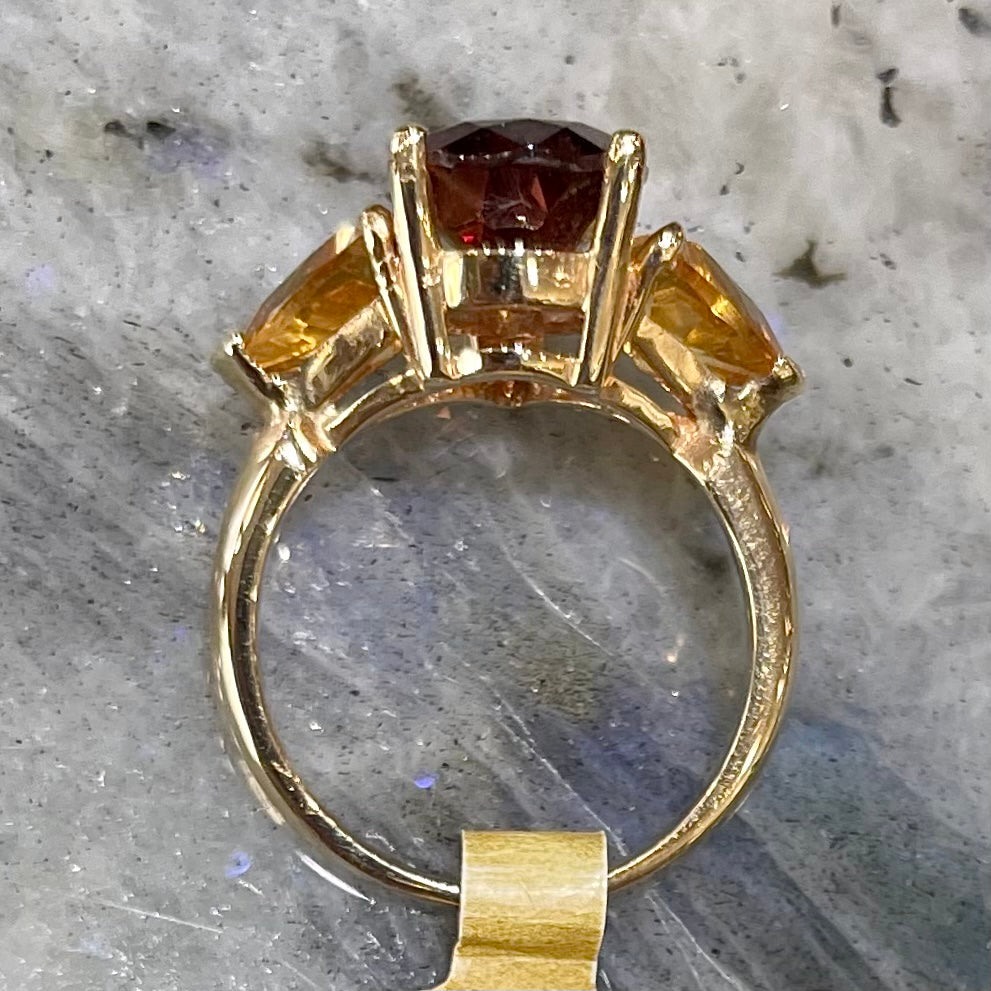 A gold ring set with a pear shape color change garnet between two trillion cut citrine accent stones.