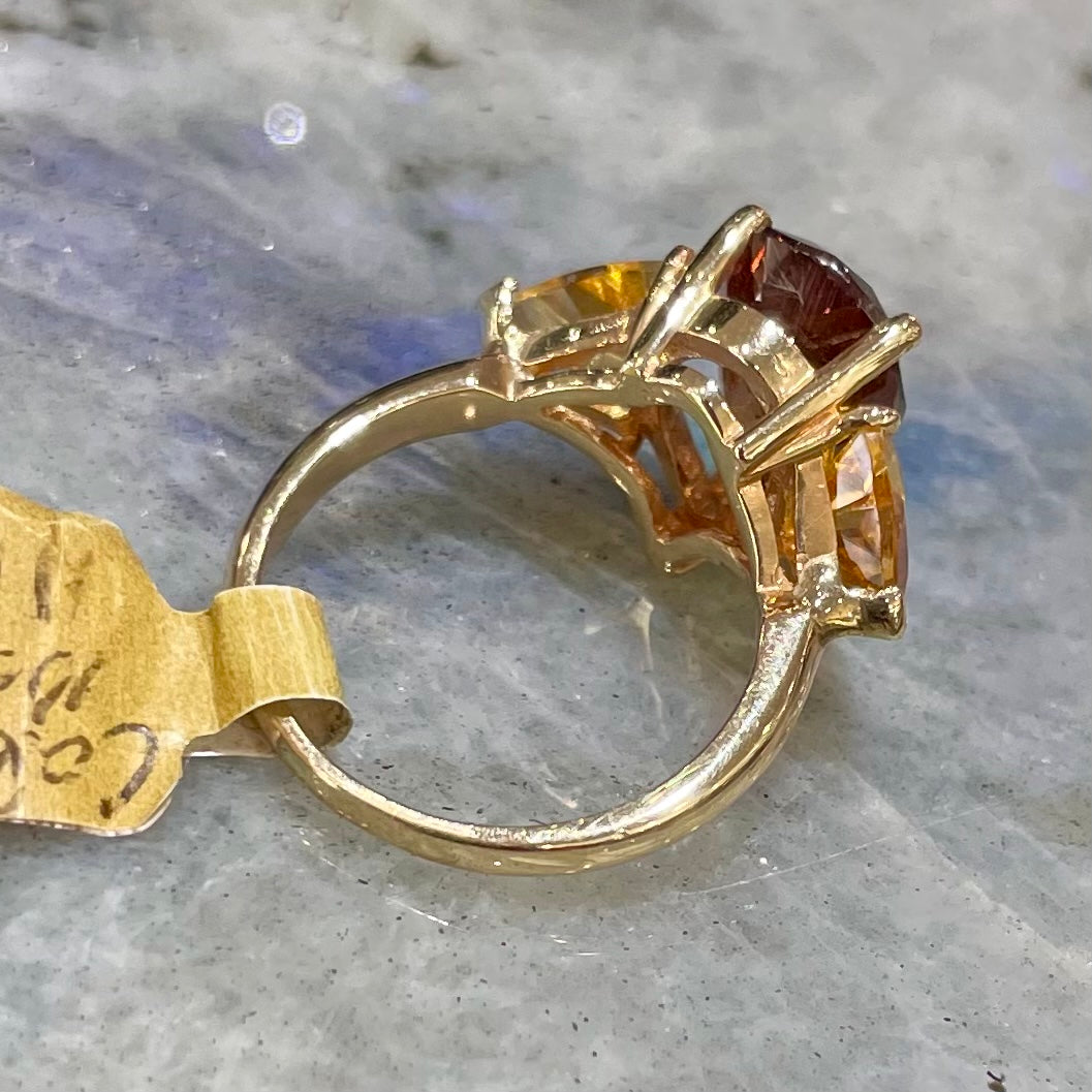 A gold ring set with a pear shape color change garnet between two trillion cut citrine accent stones.
