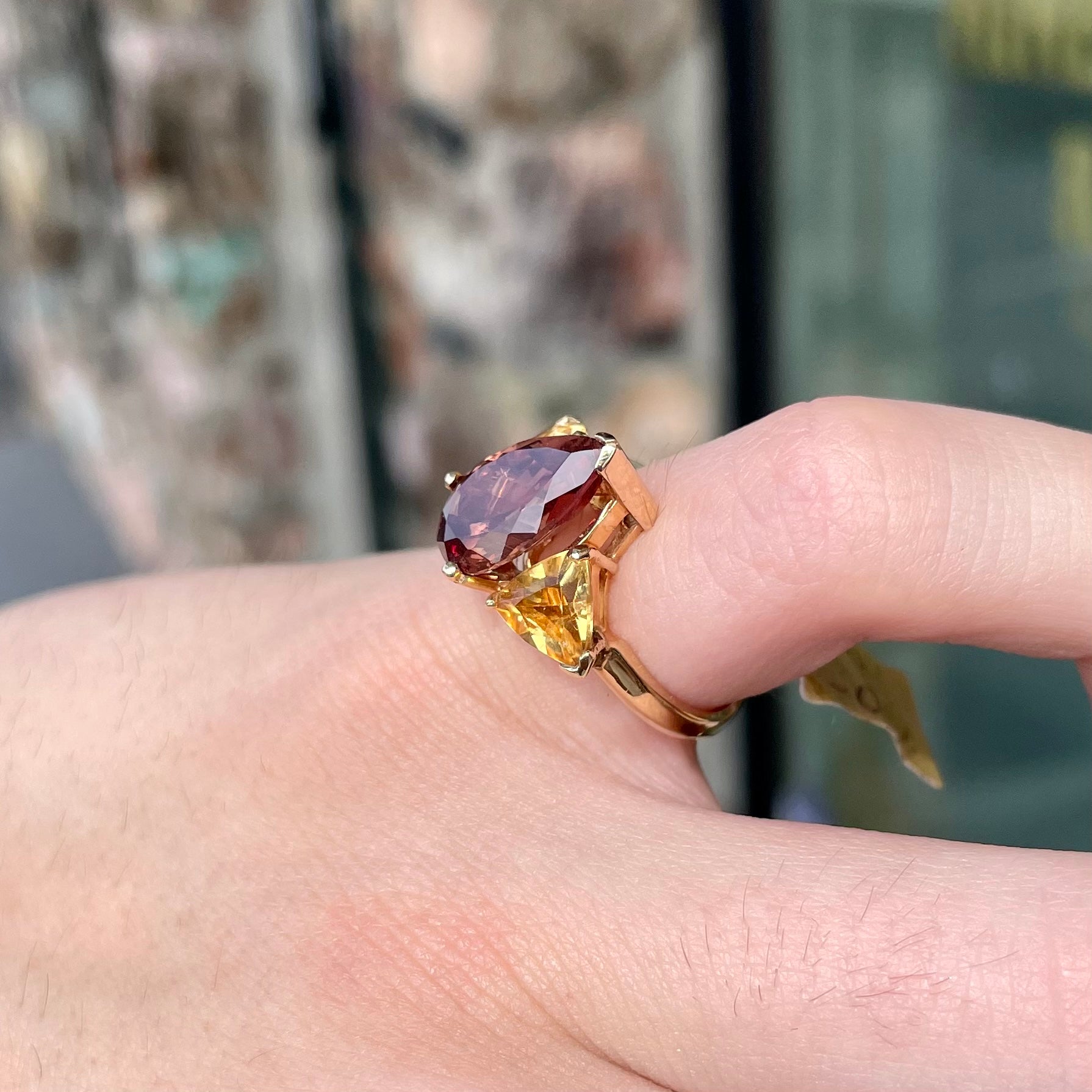 A gold ring set with a pear shape color change garnet between two trillion cut citrine accent stones.