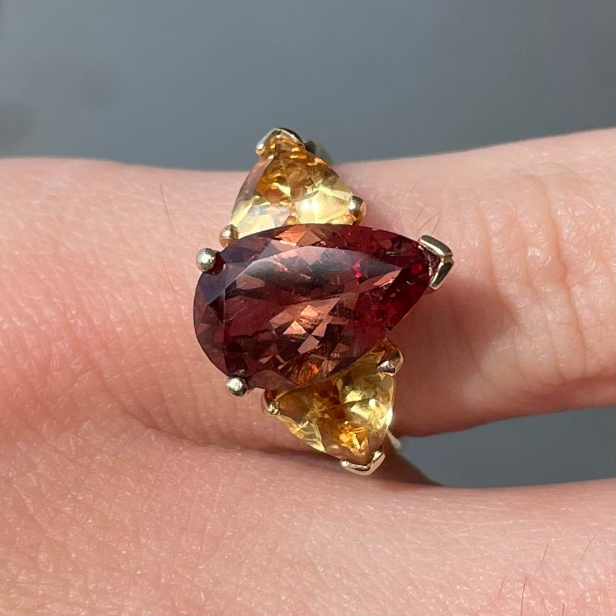 A gold ring set with a pear shape color change garnet between two trillion cut citrine accent stones.