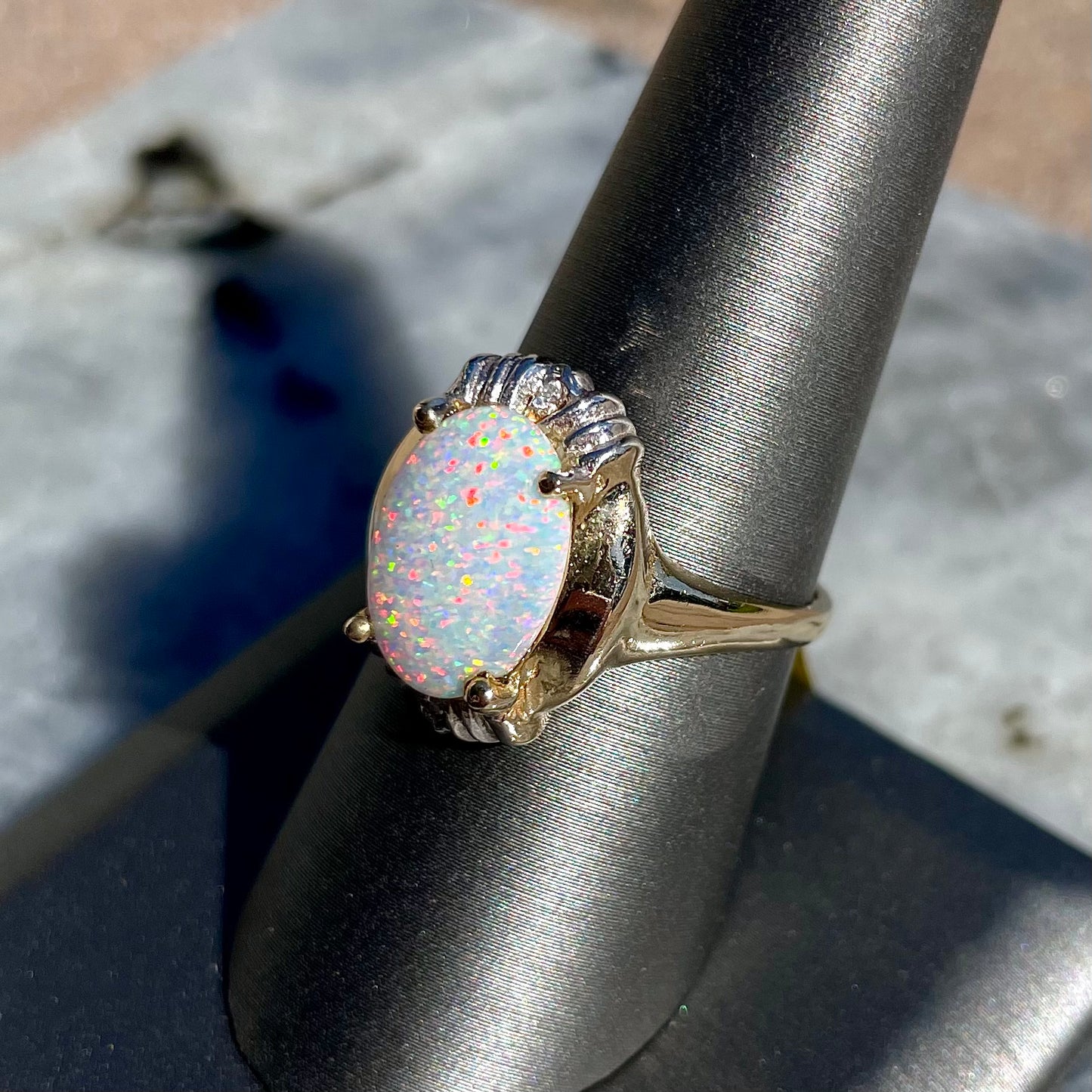A yellow gold ring set with a synthetic, lab created white opal and two natural diamond accents.