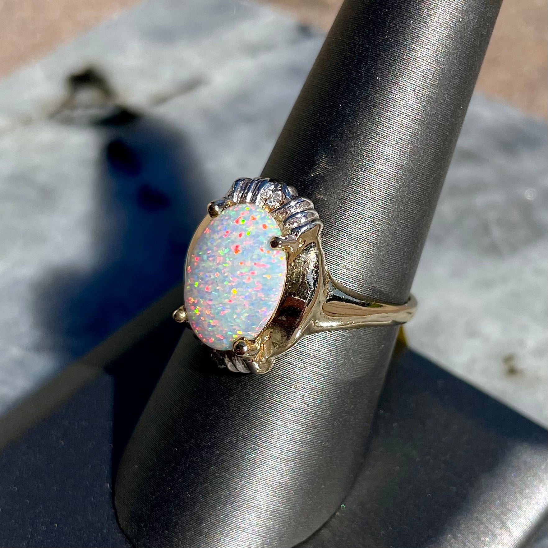 A yellow gold ring set with a synthetic, lab created white opal and two natural diamond accents.