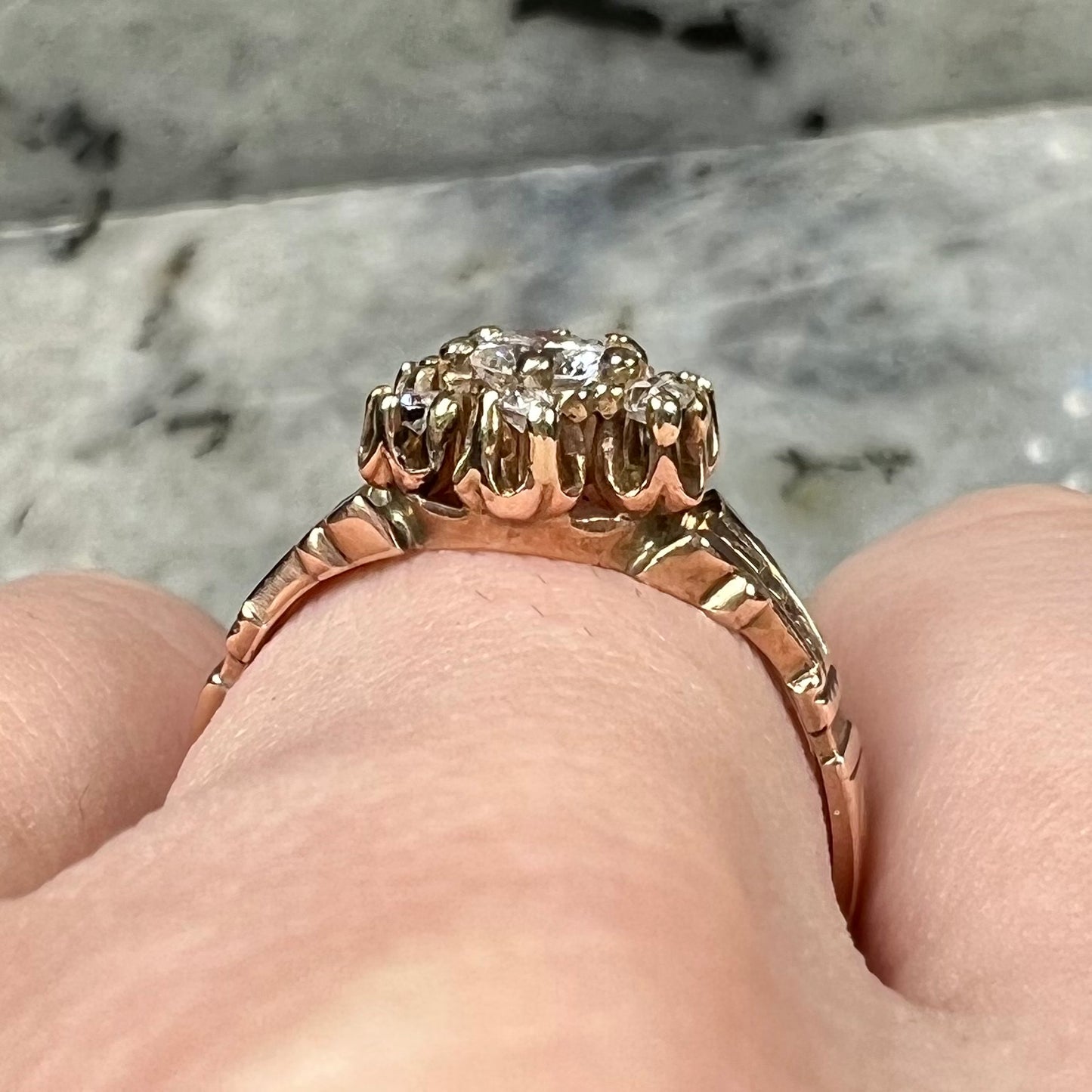 A modern Standard Round Brilliant Cut diamond set between six smaller round diamonds in an antique rose gold engagement ring setting.