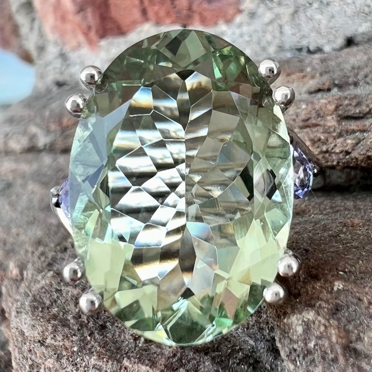 A sterling silver oval cut prasiolite ring set with two pear shaped tanzanite accent side stones.