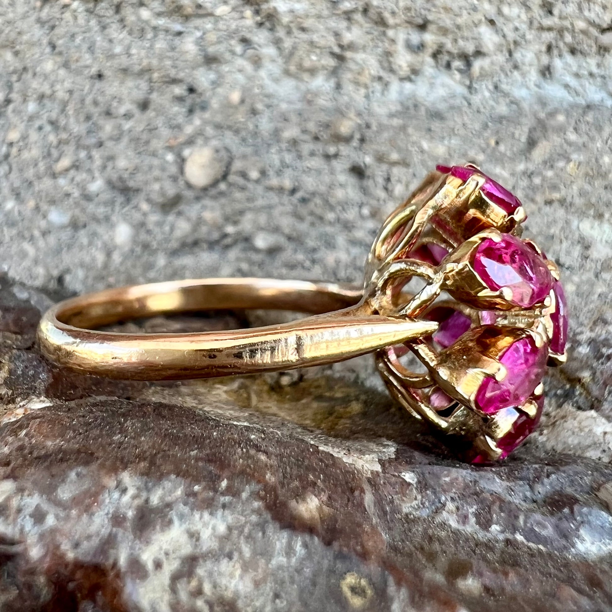 A yellow gold pink Burma ruby cluster ring with a faceted oval center stone surrounded by marquise cut stones.