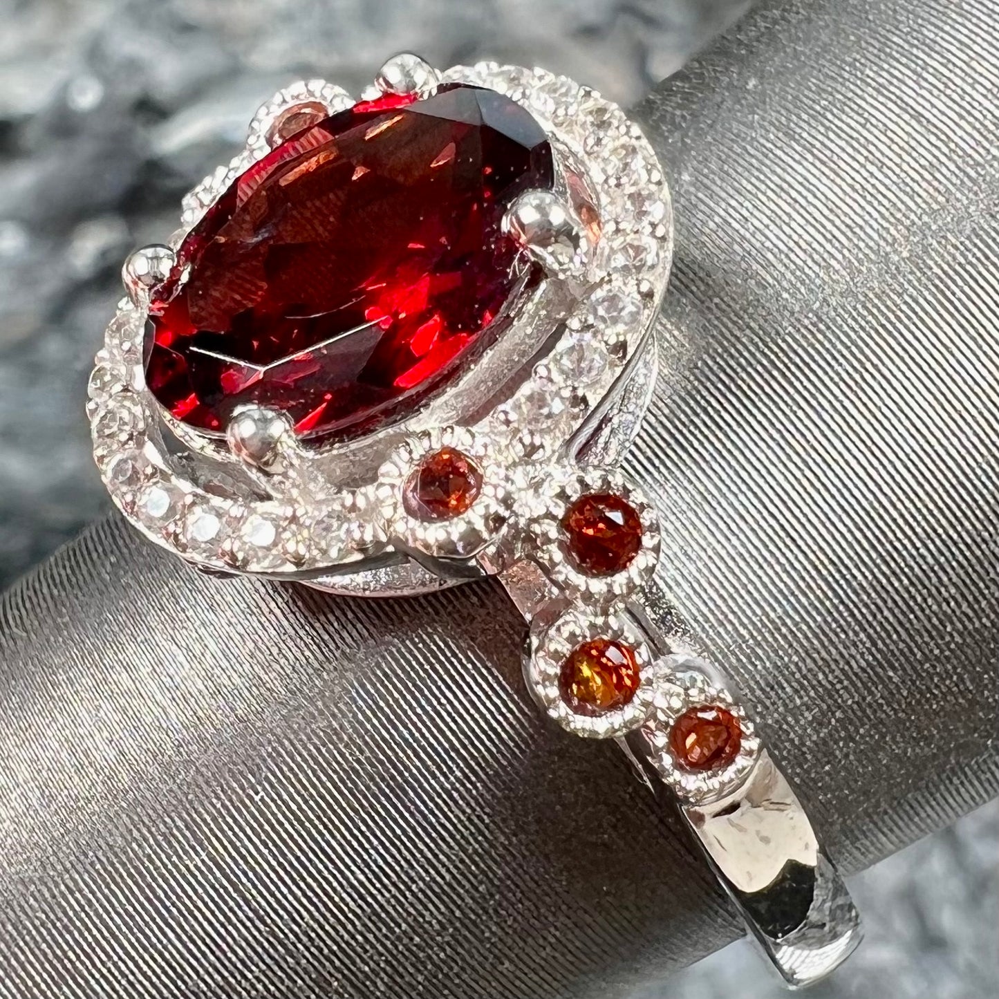 A silver garnet and CZ halo ring. The center stone is a red almandine garnet, and the side garnets are orange.