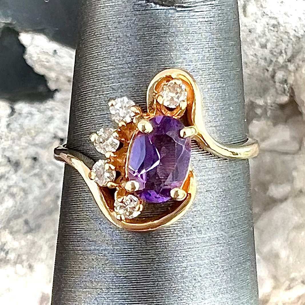 A ring made with 14 karat yellow gold, diamonds, and an amethyst. The ring has a swoosh style.