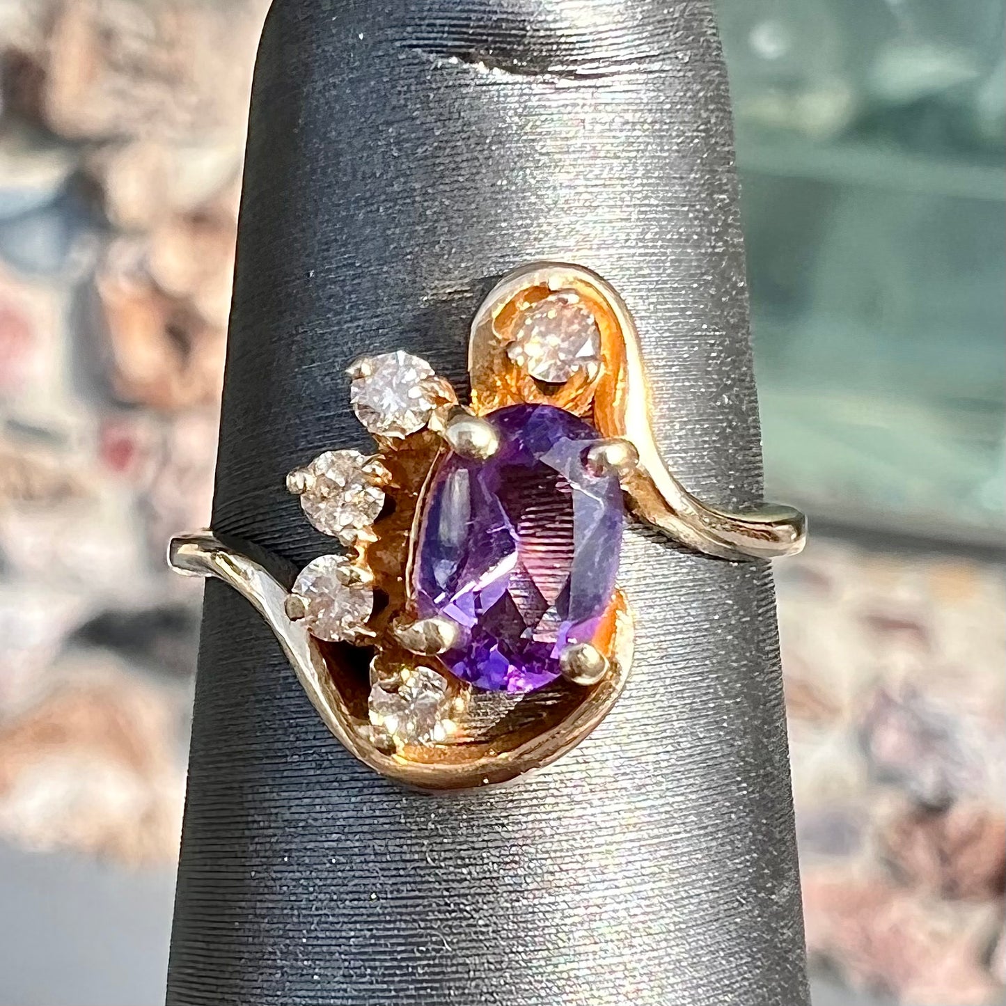 A ring made with 14 karat yellow gold, diamonds, and an amethyst. The ring has a swoosh style.