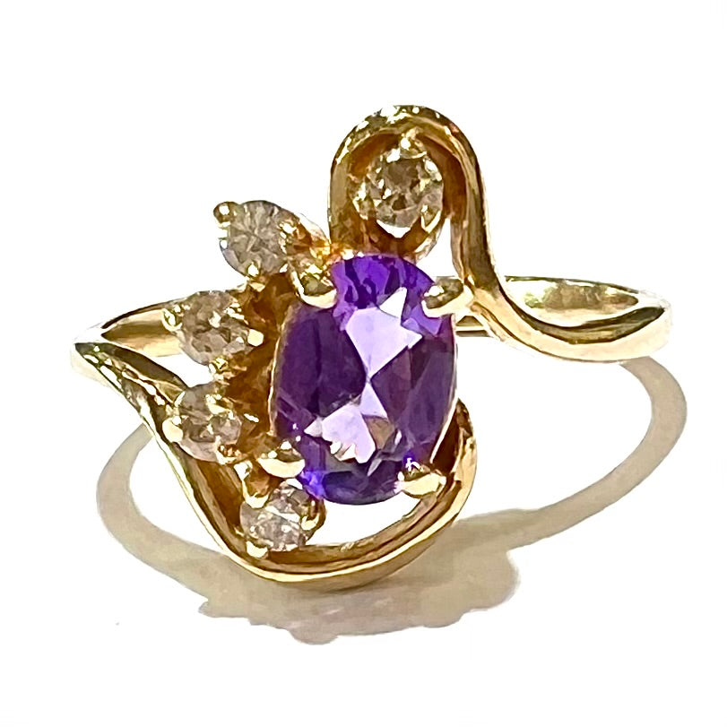 A ring made with 14 karat yellow gold, diamonds, and an amethyst. The ring has a swoosh style.