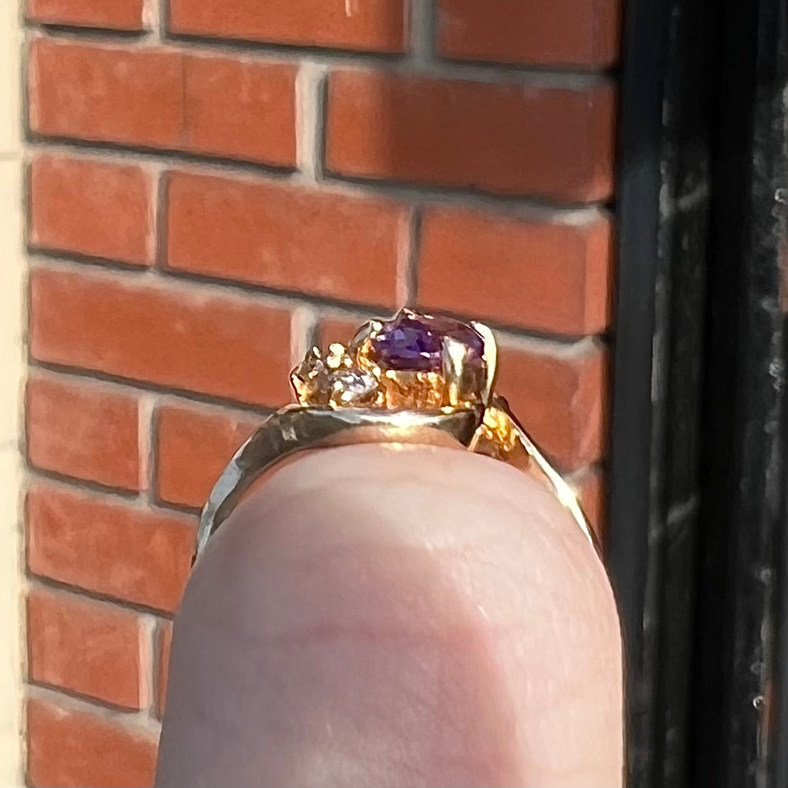 A ring made with 14 karat yellow gold, diamonds, and an amethyst. The ring has a swoosh style.