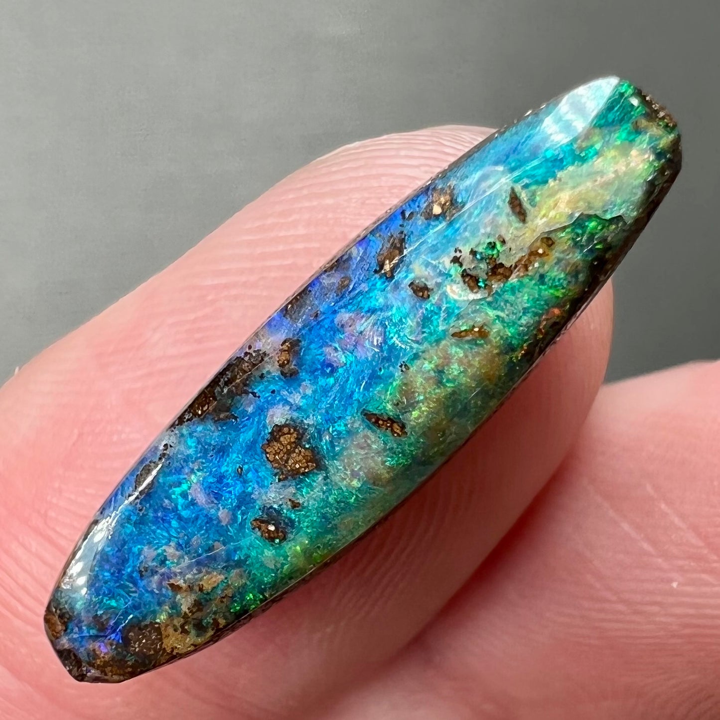 A loose, oval cabochon cut Australian boulder opal from Quilpie, Australia. Predominant colors are blue and green.