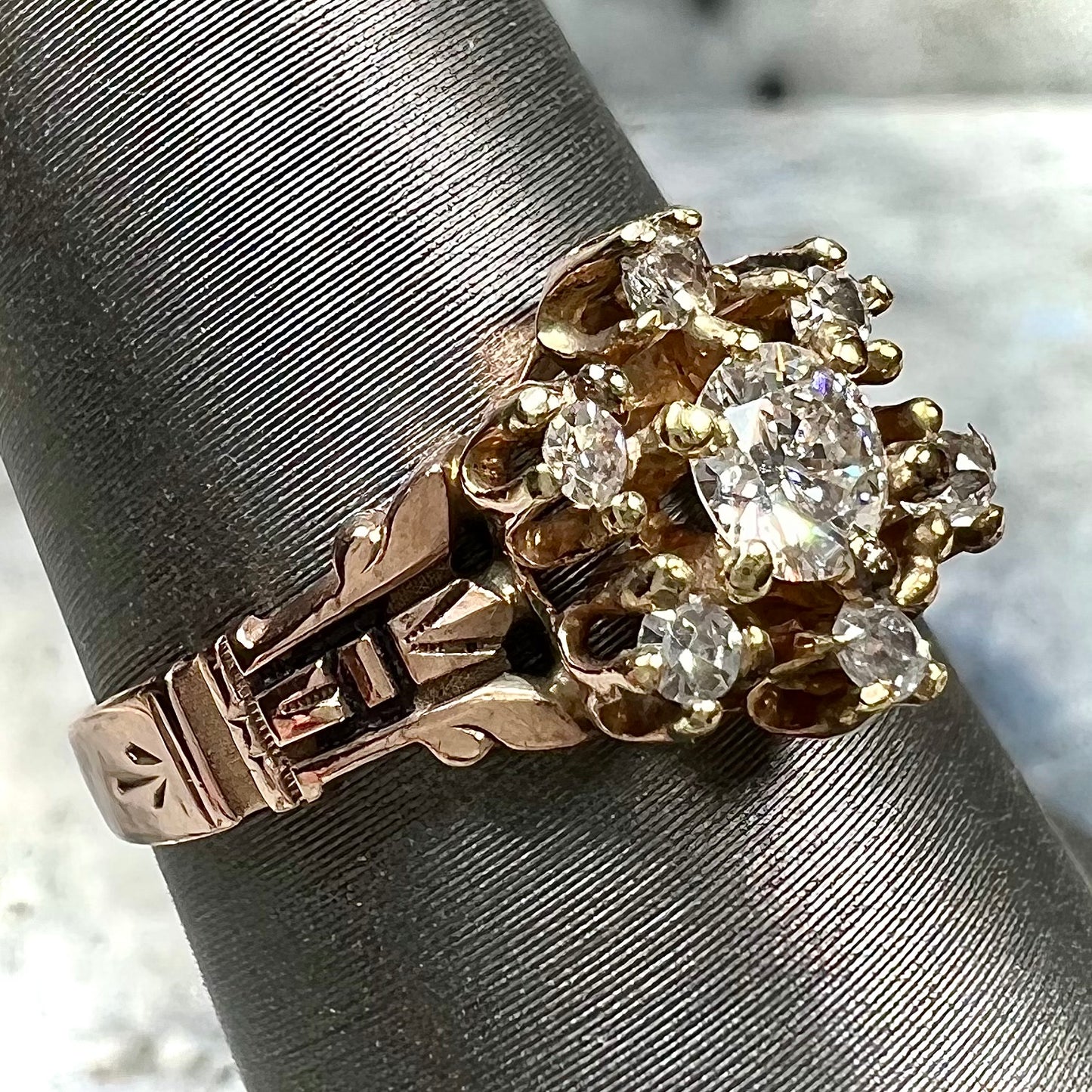 A modern Standard Round Brilliant Cut diamond set between six smaller round diamonds in an antique rose gold engagement ring setting.