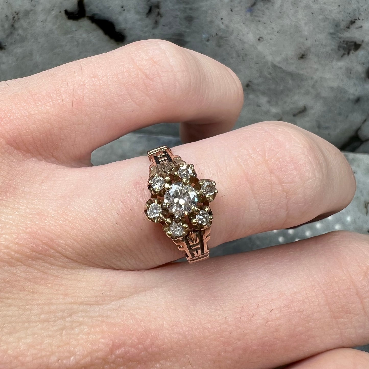 A modern Standard Round Brilliant Cut diamond set between six smaller round diamonds in an antique rose gold engagement ring setting.