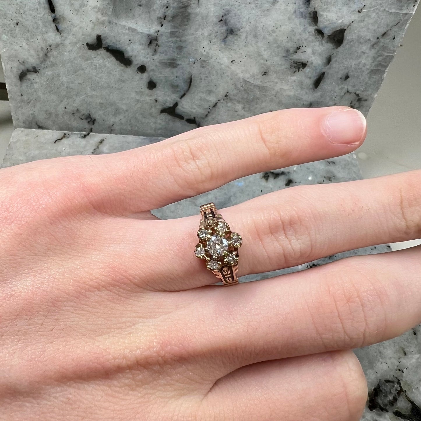 A modern Standard Round Brilliant Cut diamond set between six smaller round diamonds in an antique rose gold engagement ring setting.
