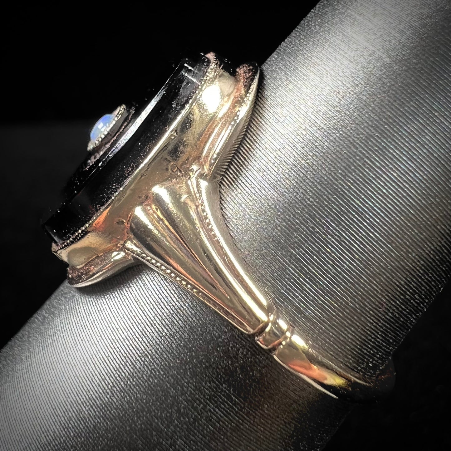 A yellow gold onyx ring set with a round cabochon cut opal bezel set into the onyx.