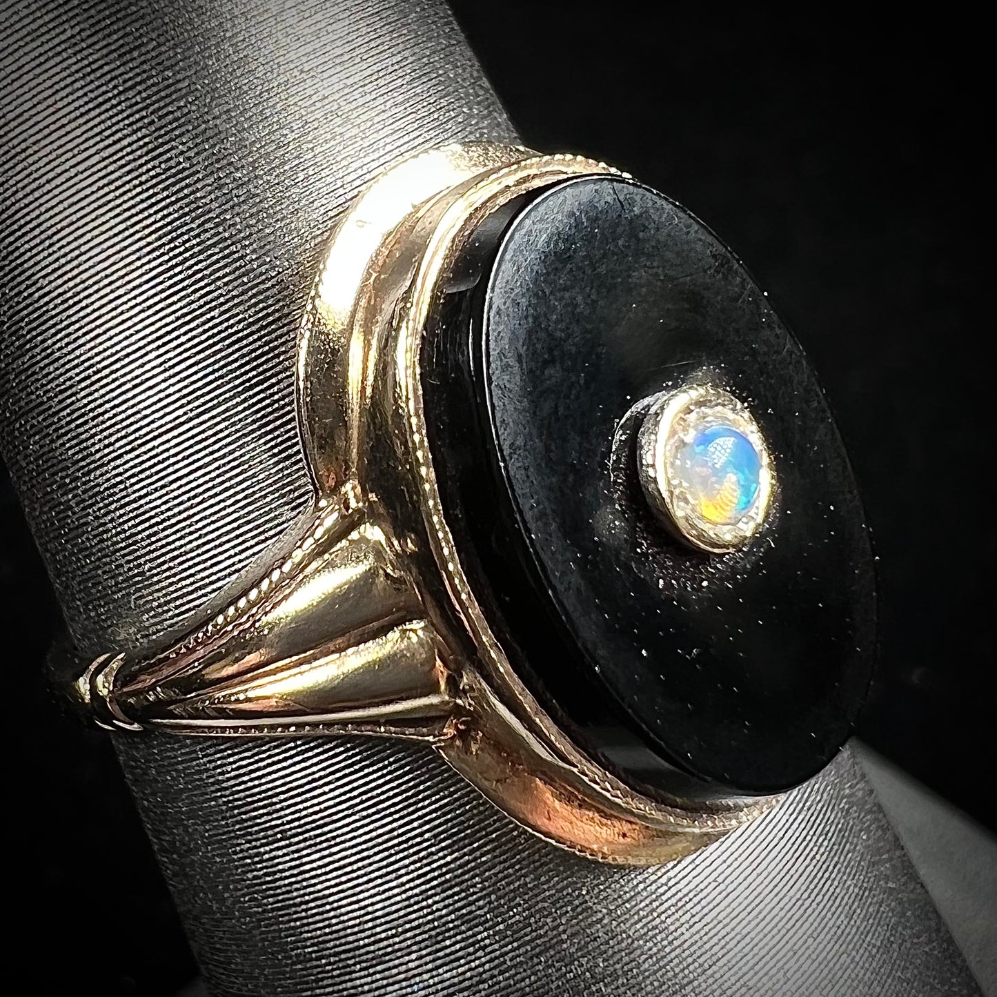 A yellow gold onyx ring set with a round cabochon cut opal bezel set into the onyx.