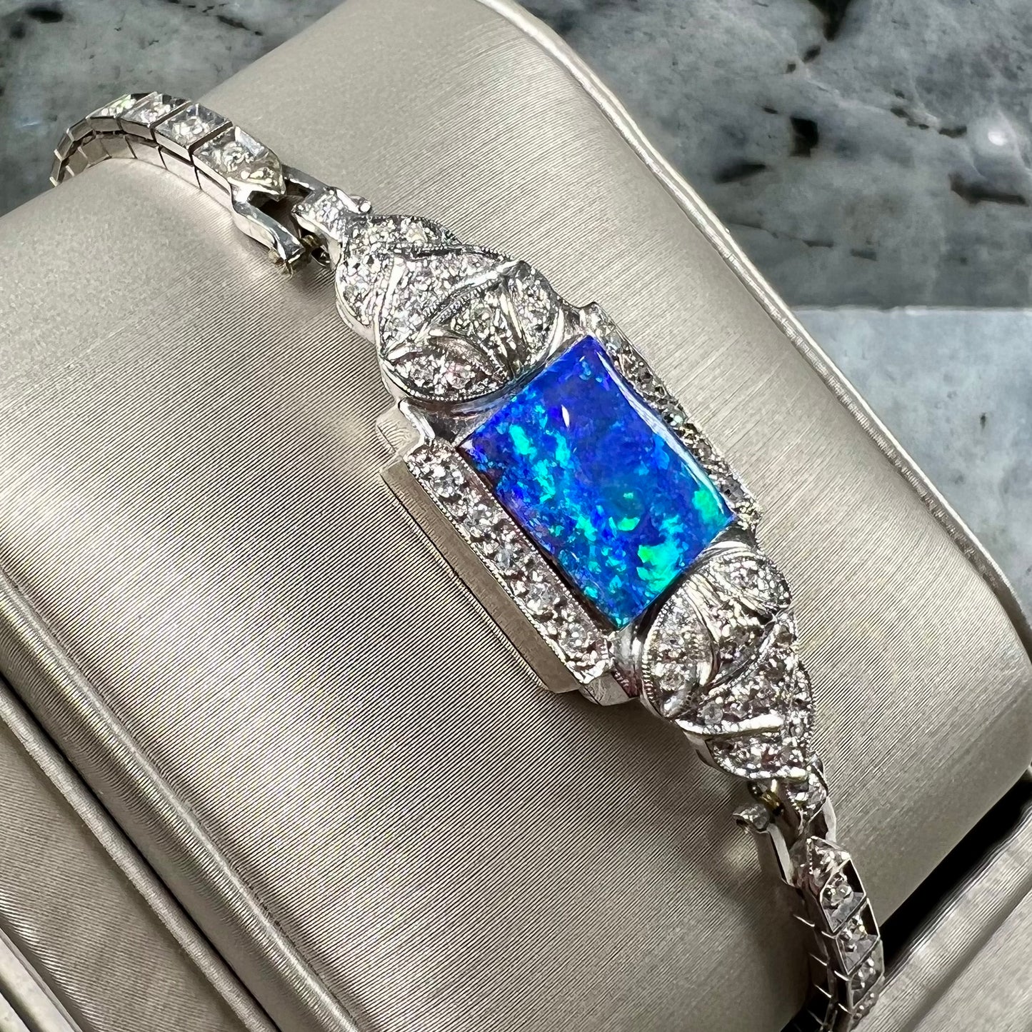 A vintage, art deco style white gold and diamond bracelet set with a rectangular shape black boulder opal stone.