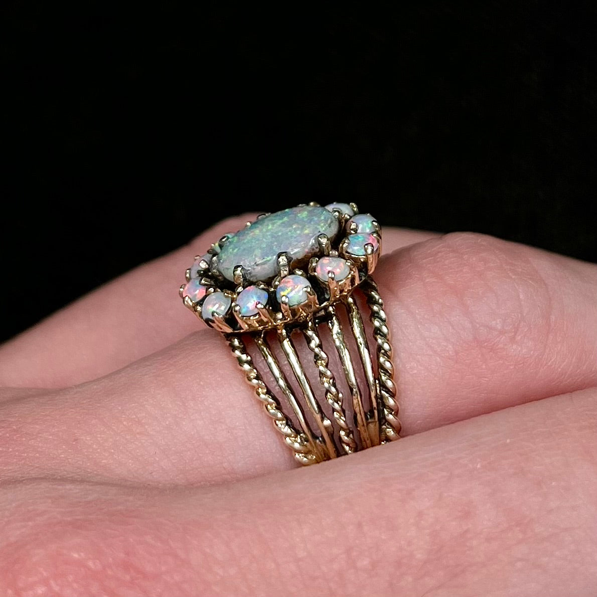 Vintage yellow gold oval opal cabochon ring set with 12 round opals in a halo around the center stone.