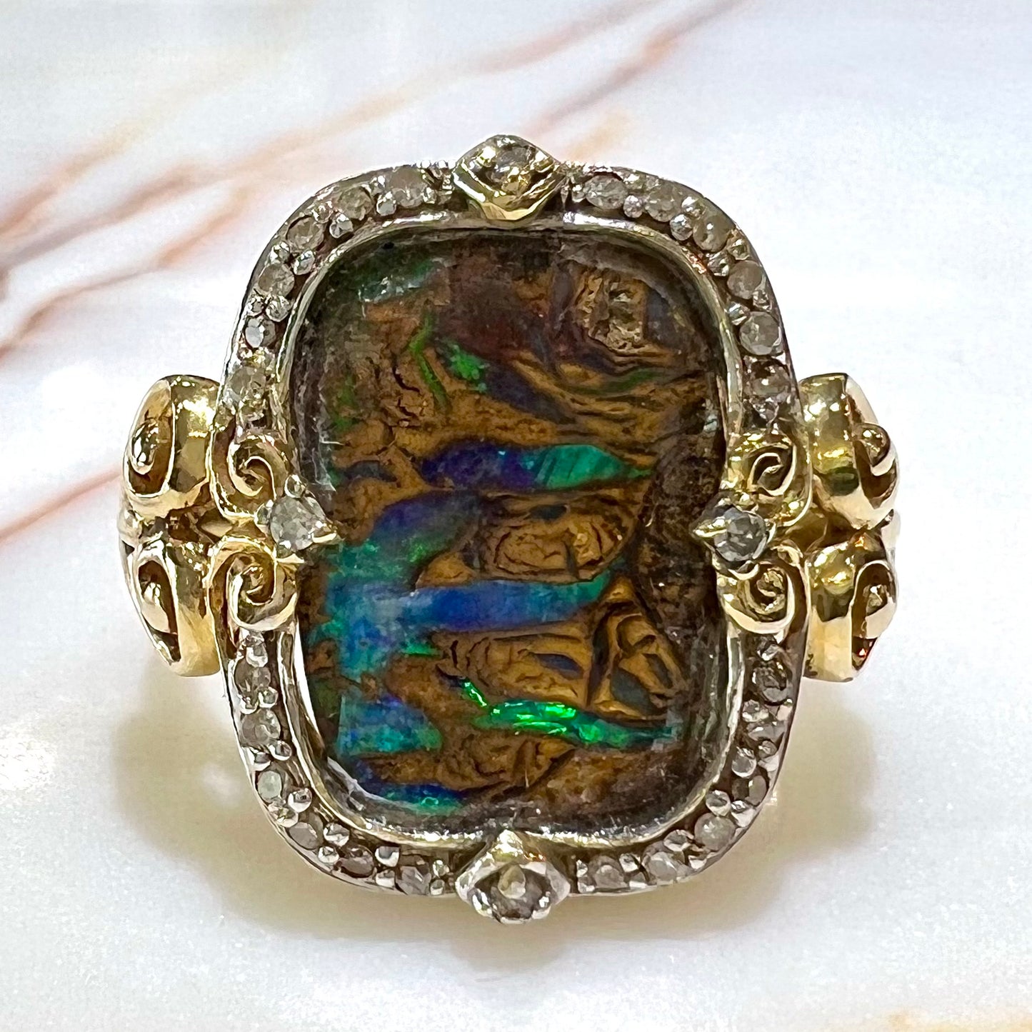 Striped Koroit boulder opal set in a filigree 14k yellow gold setting with diamonds. The filigree has a heart pattern.