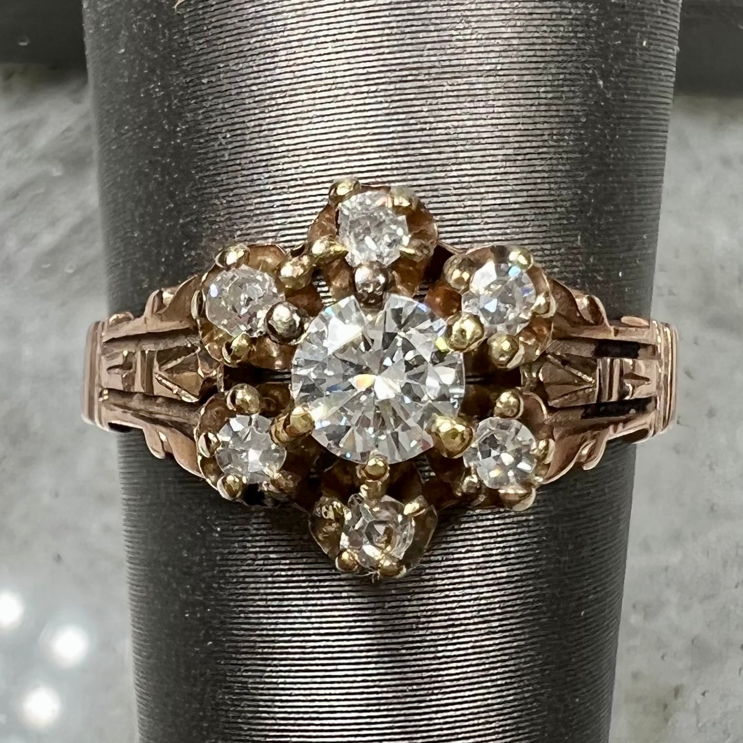 A modern Standard Round Brilliant Cut diamond set between six smaller round diamonds in an antique rose gold engagement ring setting.