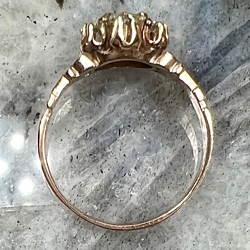 A modern Standard Round Brilliant Cut diamond set between six smaller round diamonds in an antique rose gold engagement ring setting.