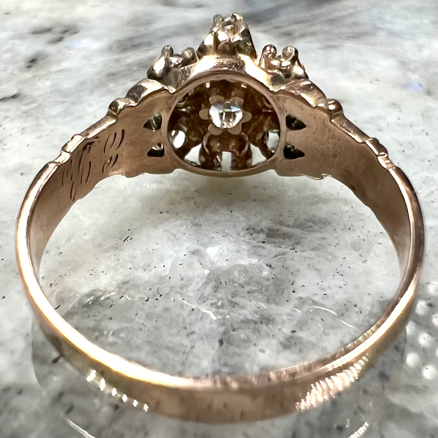 A modern Standard Round Brilliant Cut diamond set between six smaller round diamonds in an antique rose gold engagement ring setting.