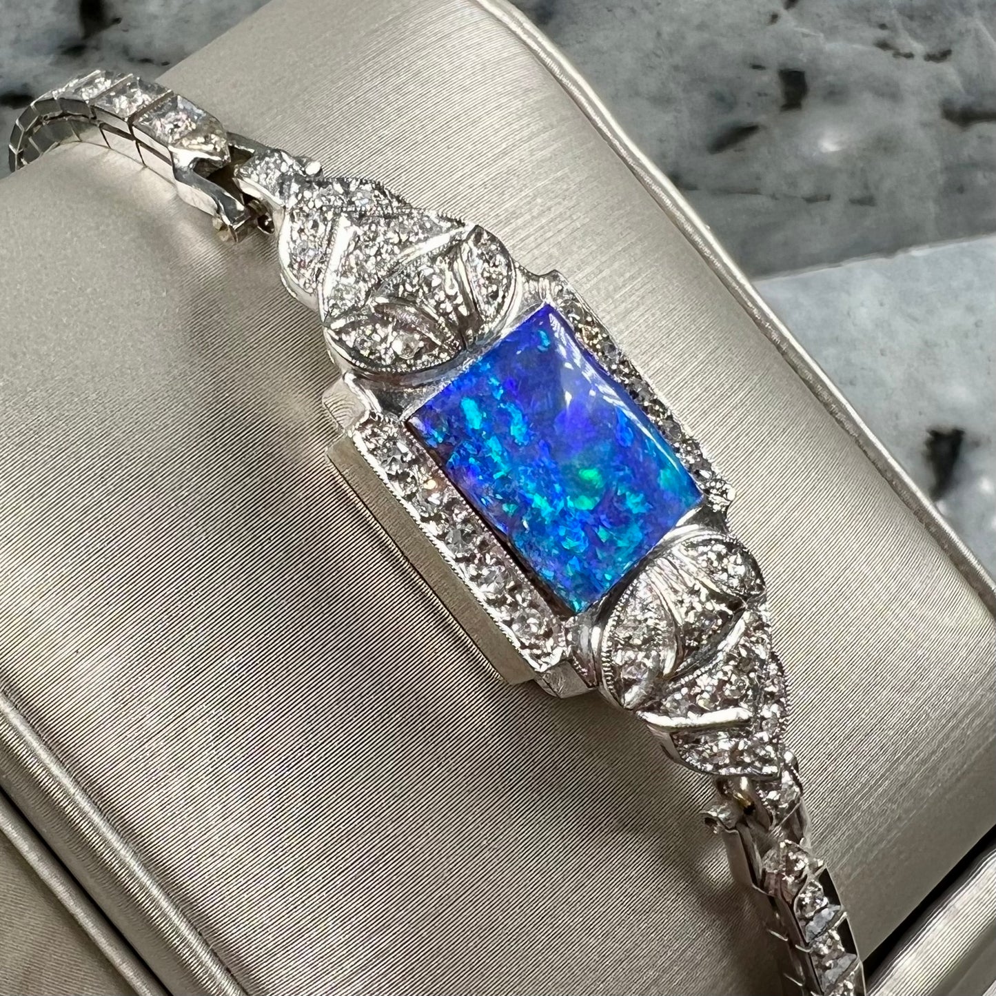 A vintage, art deco style white gold and diamond bracelet set with a rectangular shape black boulder opal stone.