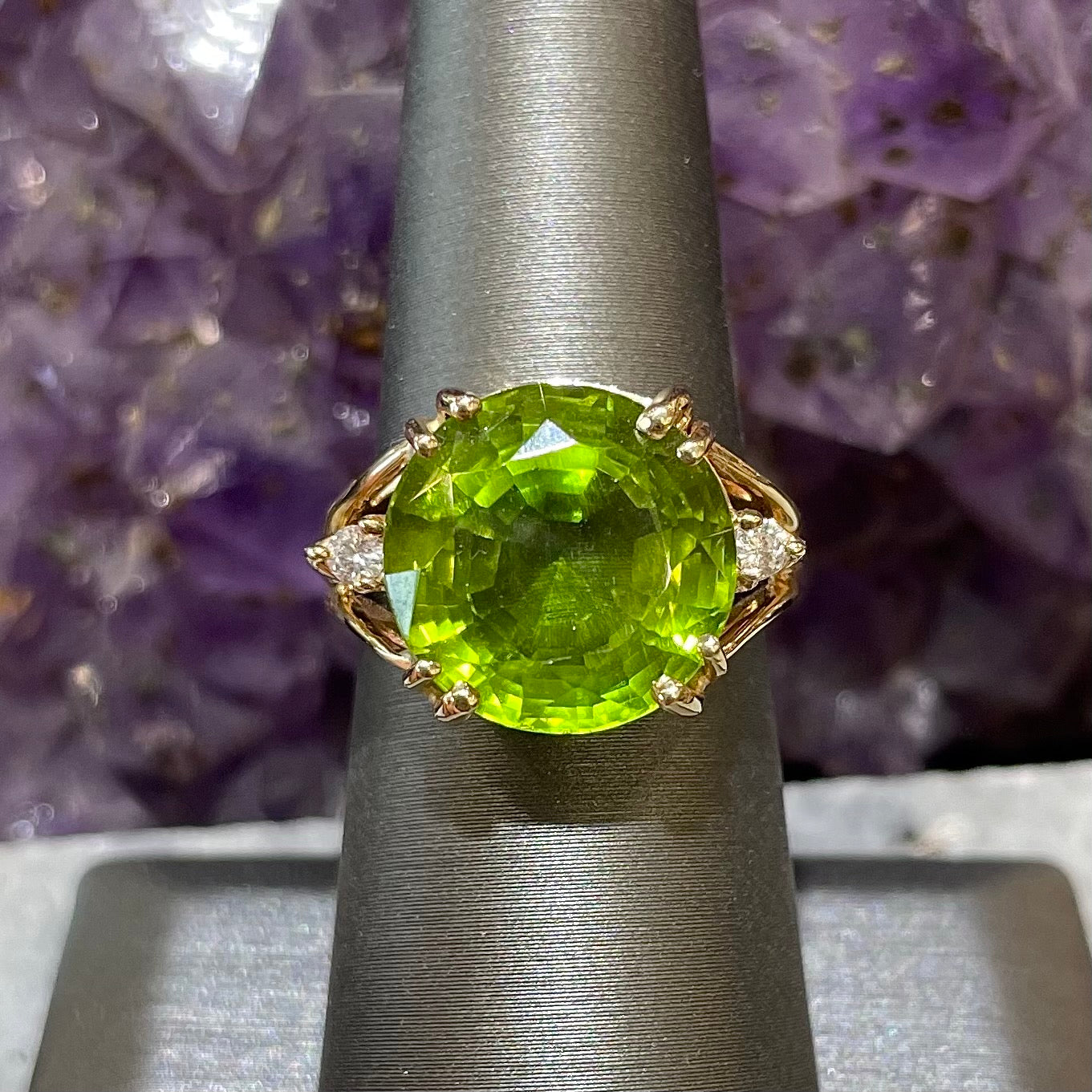 A ladies' round brilliant cut peridot statement ring set with two round diamond accents in yellow gold.