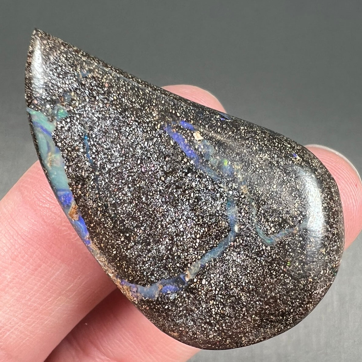 A polished pear shaped boulder opal stone from Quilpie, Australia. Predominant colors are blue, green, and aqua.