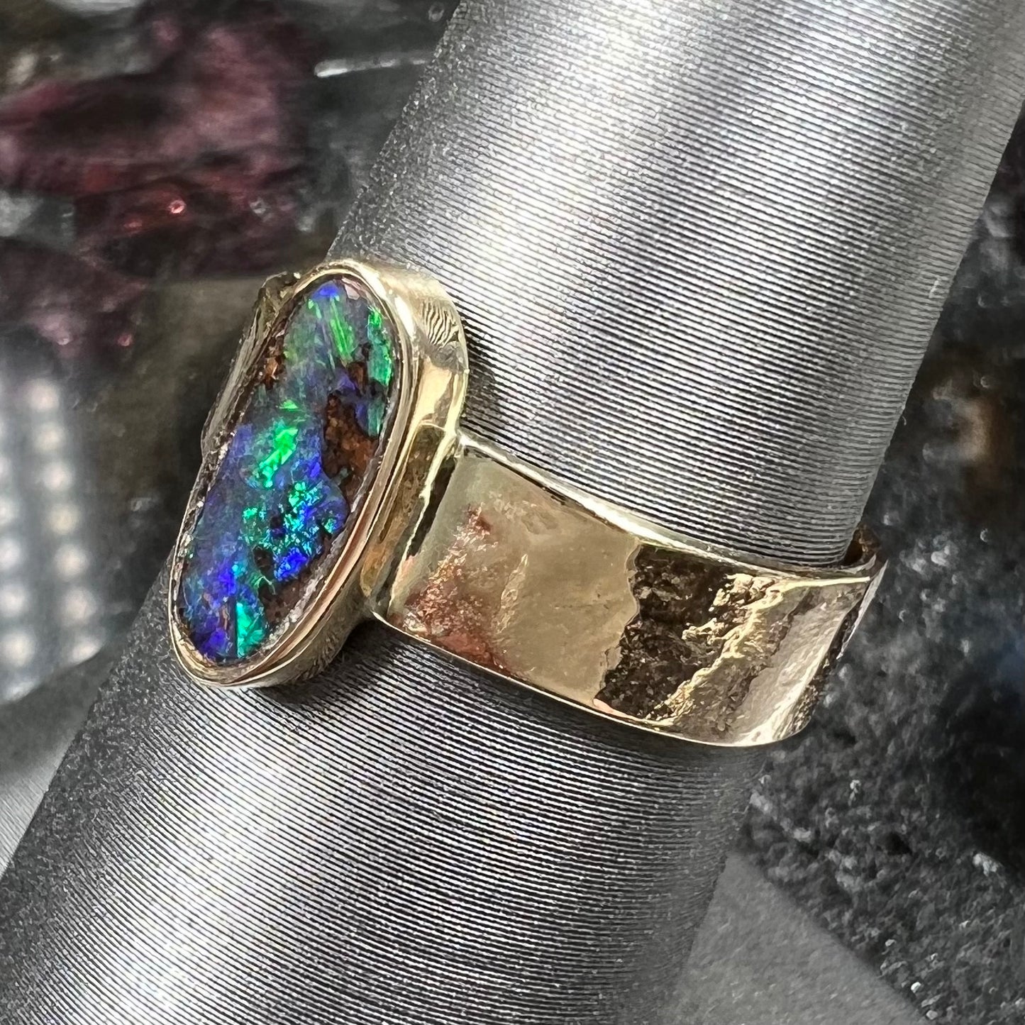 A blue green oval cabochon cut Australian boulder opal set in a yellow gold solitaire ring.