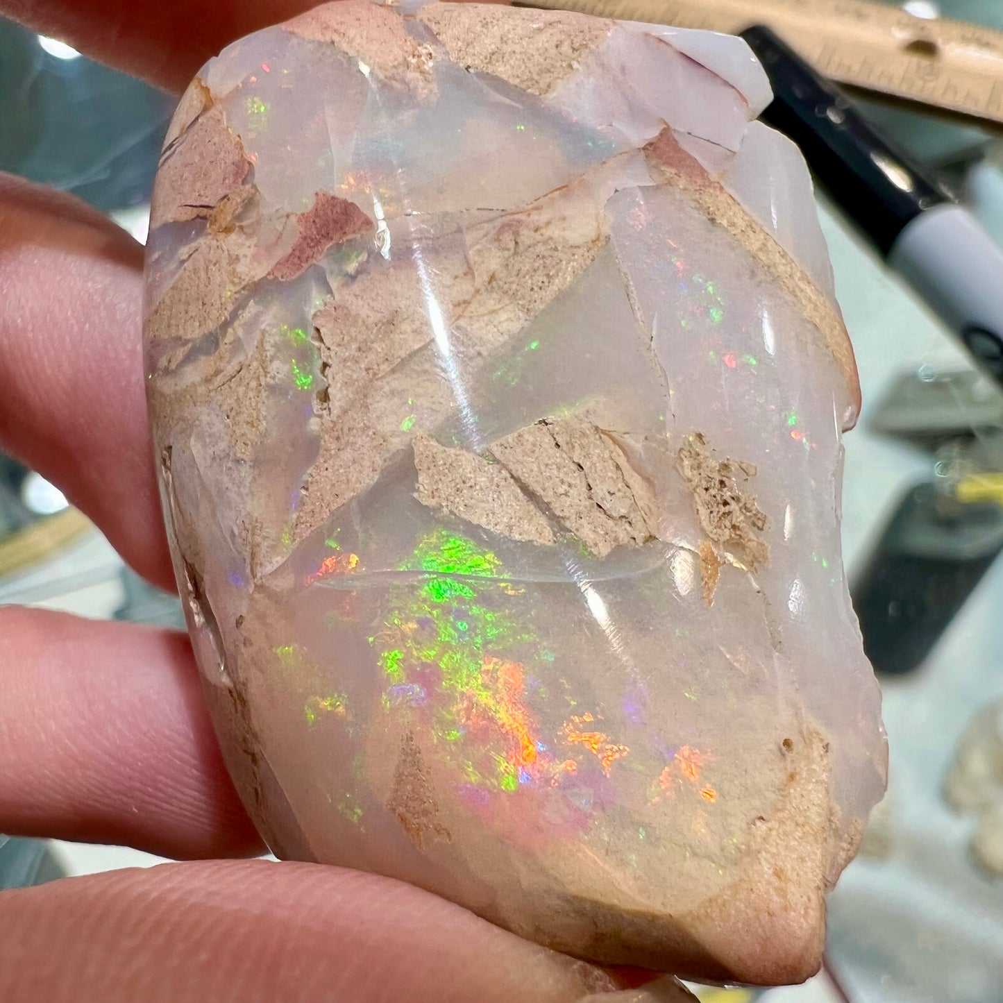 A preform polished matrix opal specimen from White Bluffs, Australia. Predominant colors are red, green, and violet.