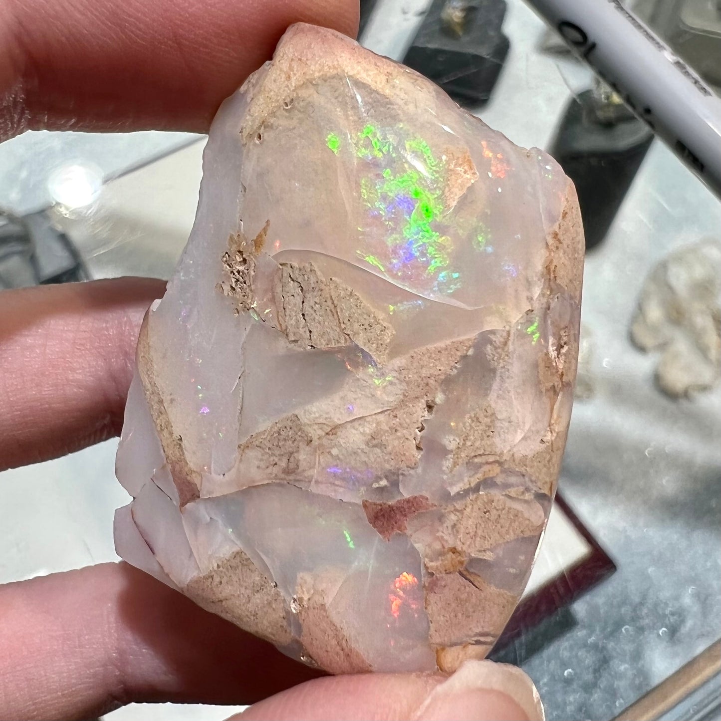 A preform polished matrix opal specimen from White Bluffs, Australia. Predominant colors are red, green, and violet.