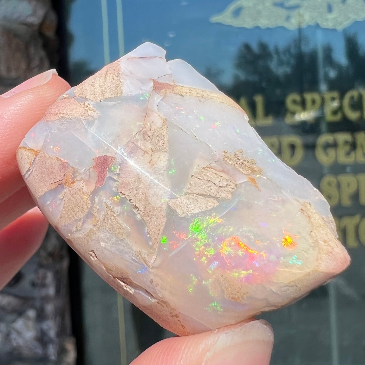 A preform polished matrix opal specimen from White Bluffs, Australia. Predominant colors are red, green, and violet.