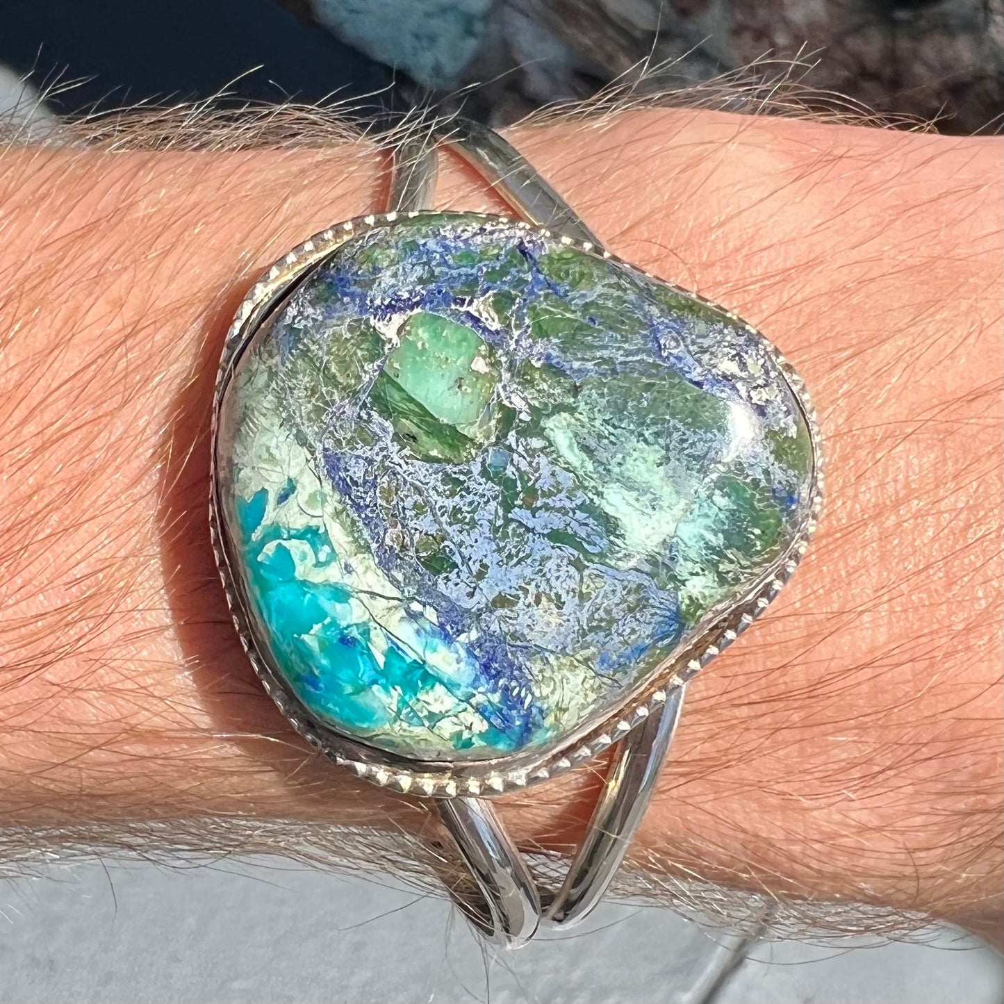 A handmade sterling silver cuff bracelet set with a single stone formed from variscite, chrysocolla, and azurite.
