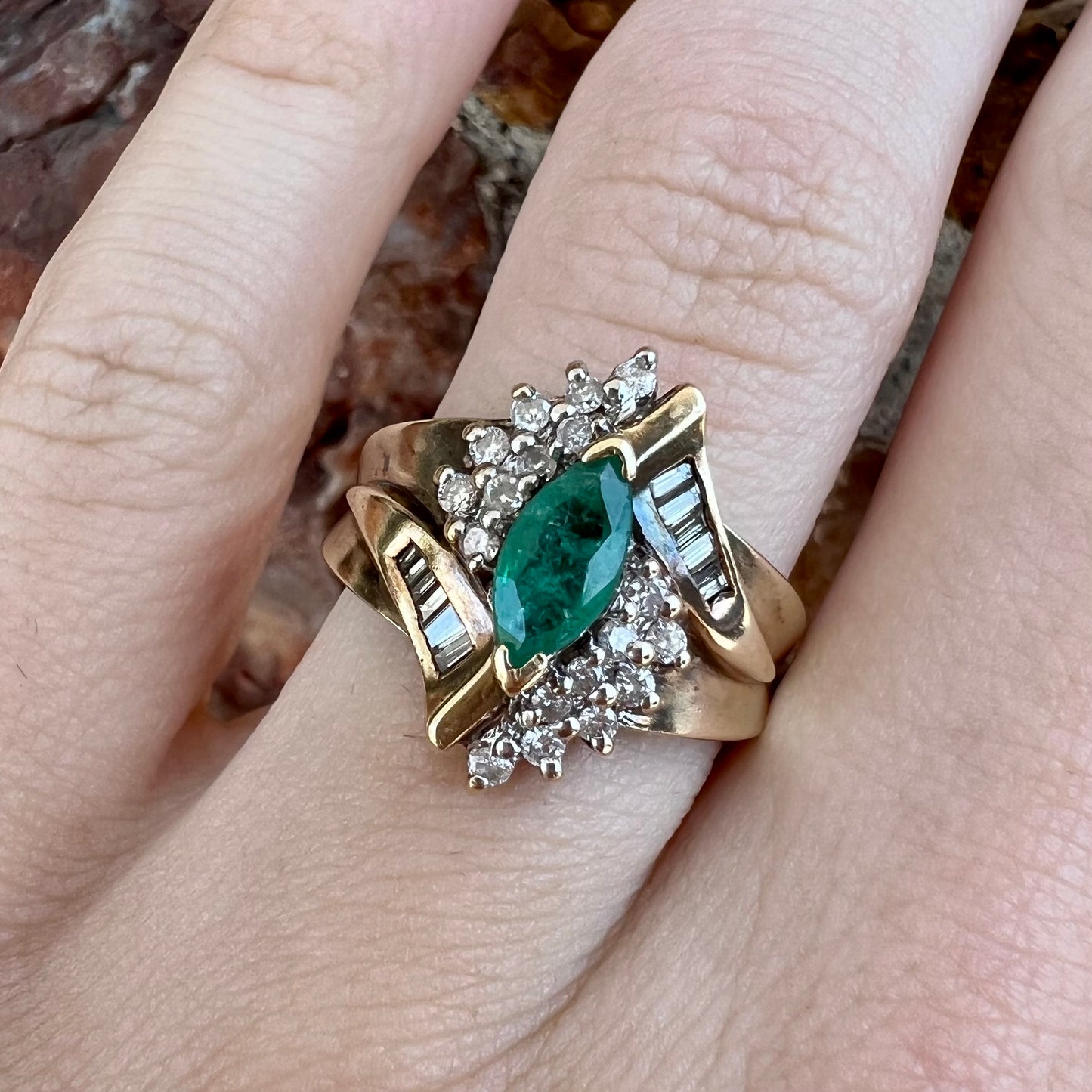 A yellow gold marquise cut emerald and diamond ring. The diamonds are prong set round cuts and channel set baguette cuts.